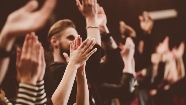 Group of people clapping hands in the theater, close up of hands. Dark tone.