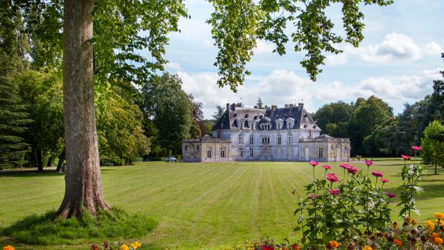 photo du parc du château d'Acquigny avec ses arbres feuillus et ses fleurs sous le ciel bleu