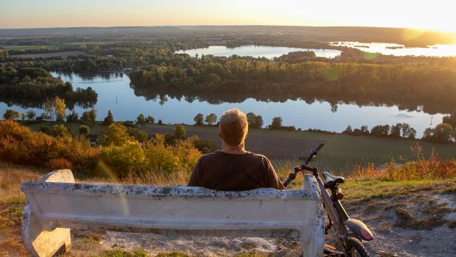 cycliste sur un banc admirant le couché de soleil et la vue sur la seine et un lac du haut du panorama de plessis dans l'Eure en Normandie