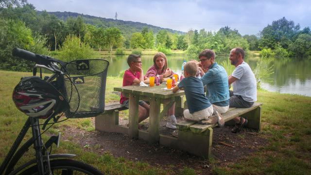 Photo d'une famille à vélo faisant une pause pique nique sur une table de pique nique au bord d'un lac dans l'Eure en Normandie