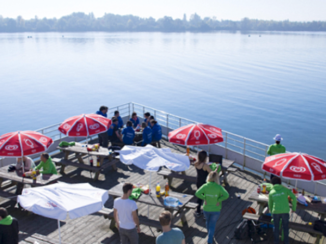 Terrasse en bois sur laquelle se restaurent des gens au bord du lac de la base des loisirs de Léry-Poses en Normandie